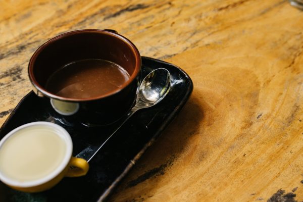 A cup of hot espresso in a dark cup on a black saucer with milk separately